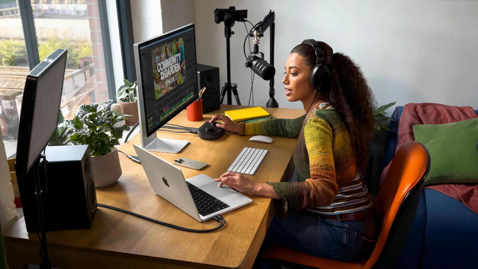 A person works with a silver 14-inch Apple MacBook Pro beside an external display and podcast recording equipment.