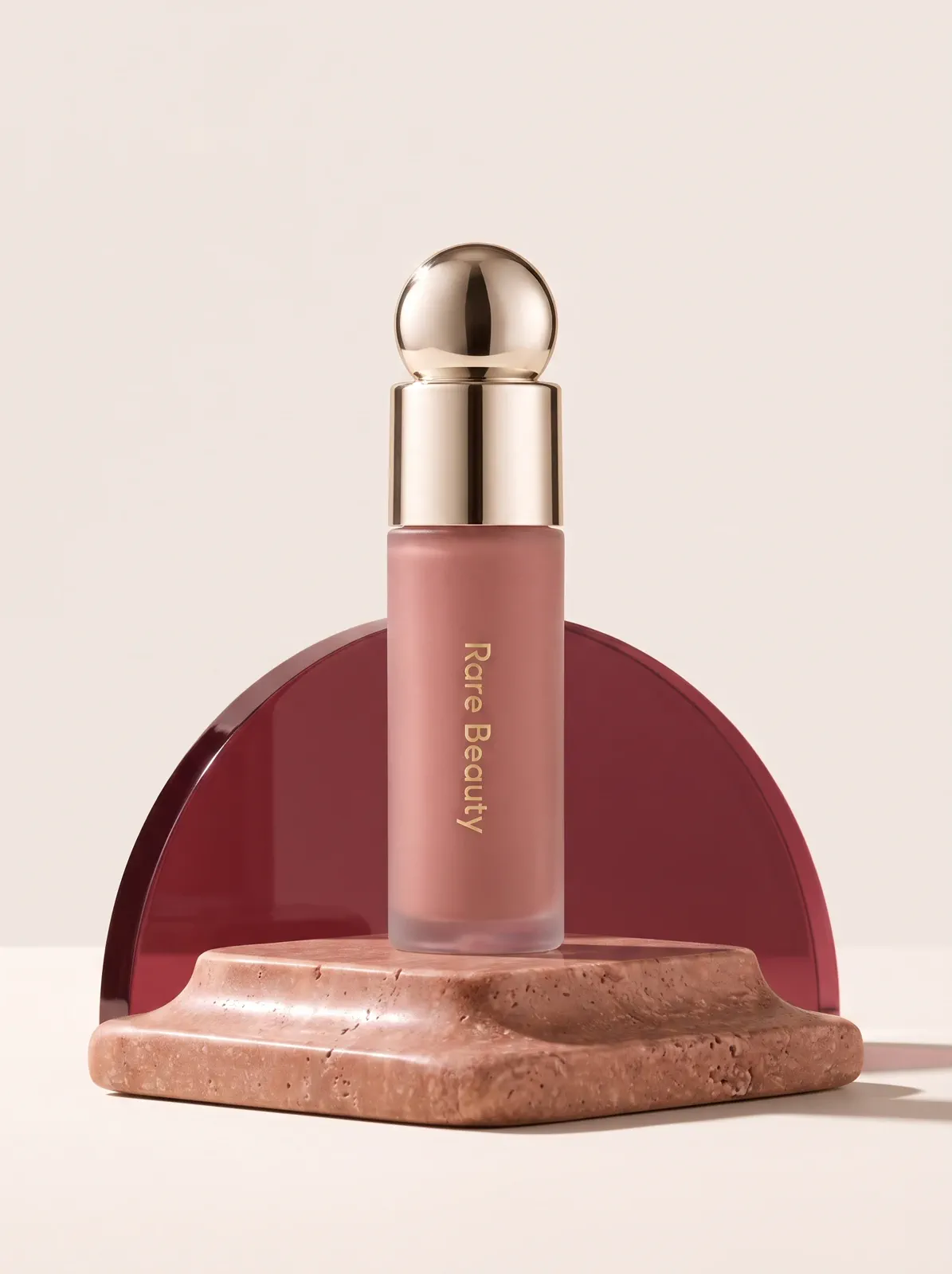 A nude-mauve liquid blush bottle in a warm rose editorial product scene.